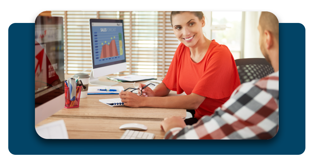 A professional consultant sitting in a bright office, smiling and pointing toward a laptop screen while explaining financial charts to a client